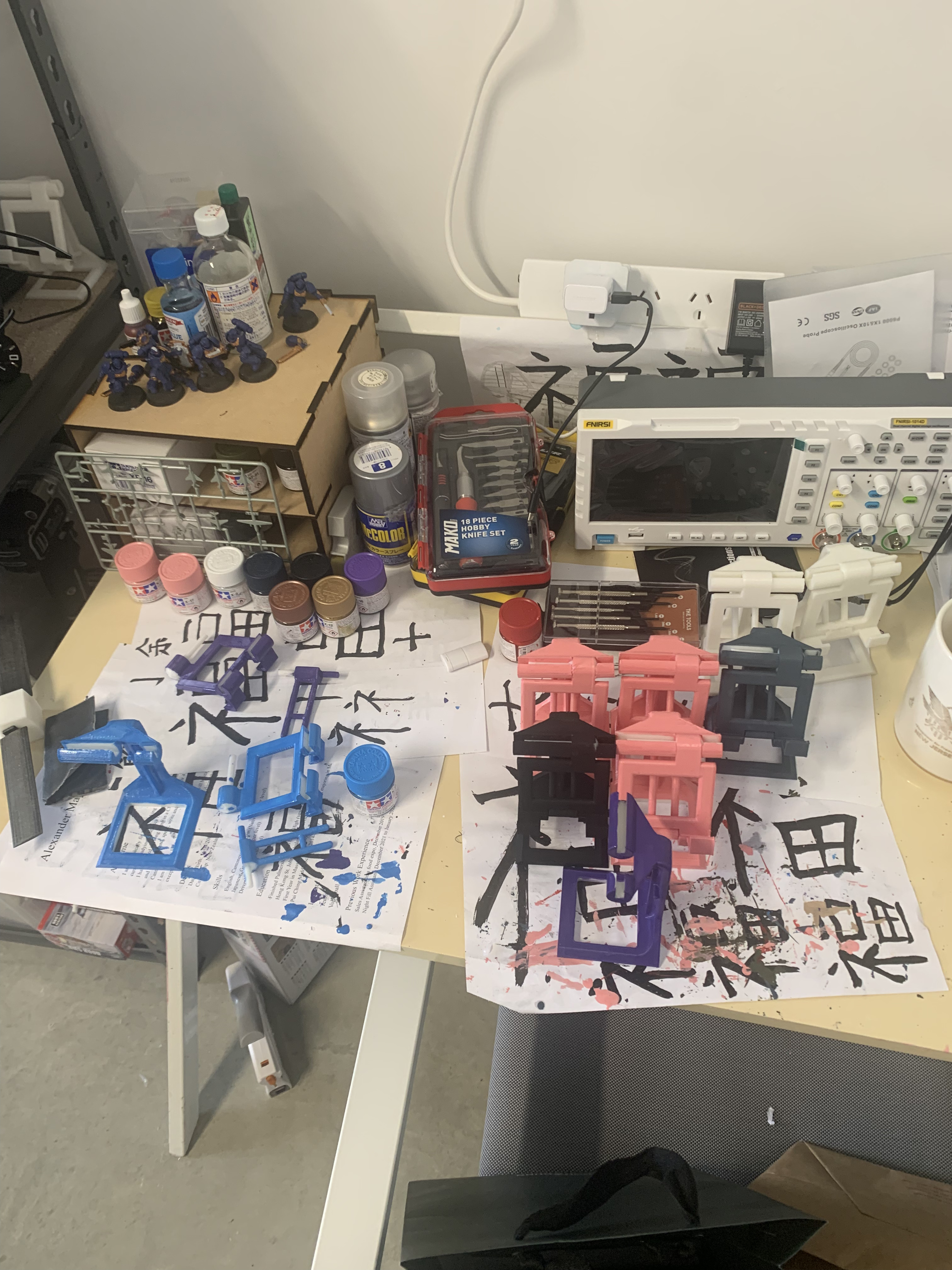 Multiple 3D-printed phone stand iterations in different colours laid out on a workbench